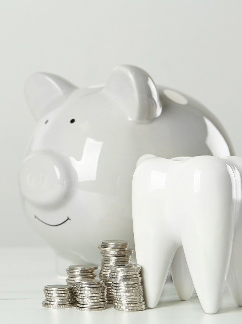 Off-white piggy bank next to large model tooth and piles of coins
