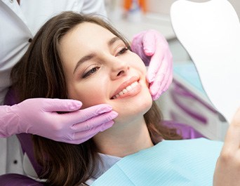 Woman in dental chair smiling at reflection in mirror as dentist touches her cheeks