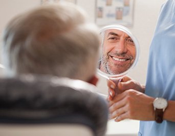 Man smiling while looking at reflection in handheld mirror