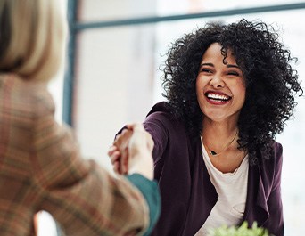 Woman in business casual smiling and shaking hands with interviewer