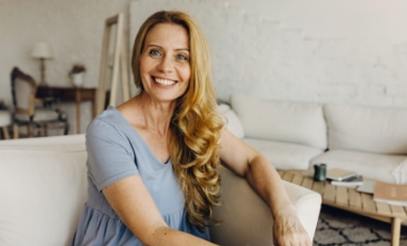 Blonde woman holding a clear aligner and pointing to her smile